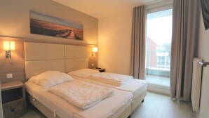 A hotel room with two beds, a headboard, bedside lamps, a painting on the wall, and a view through the window.