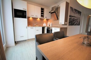 Une cuisine moderne avec des meubles blancs, un four encastré et un coin repas comprenant une table en bois et deux chaises.