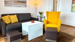 Una sala de estar moderna con un sofá negro, un sillón amarillo, una mesa de centro blanca y una alfombra marrón.