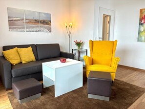 A modern living room with a black sofa, a yellow armchair, a white coffee table, and a brown rug.