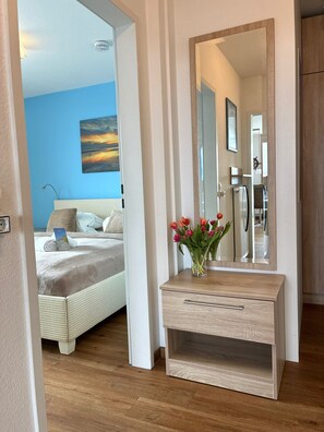 Ein Schlafzimmer mit einem Bett, einem Nachttisch mit Blumenvase, einem großen Spiegel und einer blauen Wand.