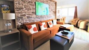 Una sala de estar con una pared de piedra, un sofá marrón con almohadones decorativos, una mesa de centro con un cuenco de bayas y una estantería con libros y una lámpara.
