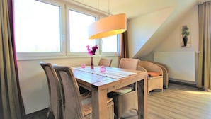 Comedor con mesa de madera, sillas de mimbre, lámpara colgante y ventanas amplias con cortinas.