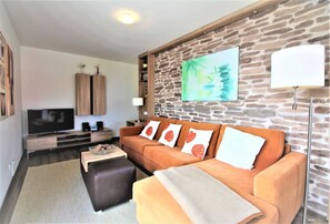 Un salon avec un mur en pierre, un téléviseur à écran plat, un canapé agrémenté de coussins décoratifs et une lampe.