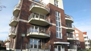 Un edificio residencial de varios pisos con balcones, una entrada central y fachada de ladrillo.