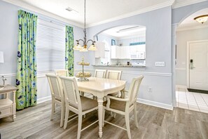 A dining area with a round table, six chairs, and a chandelier.