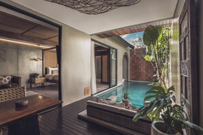 Un interior moderno con una terraza de madera, una piscina y vistas a un muro de ladrillo y follaje.