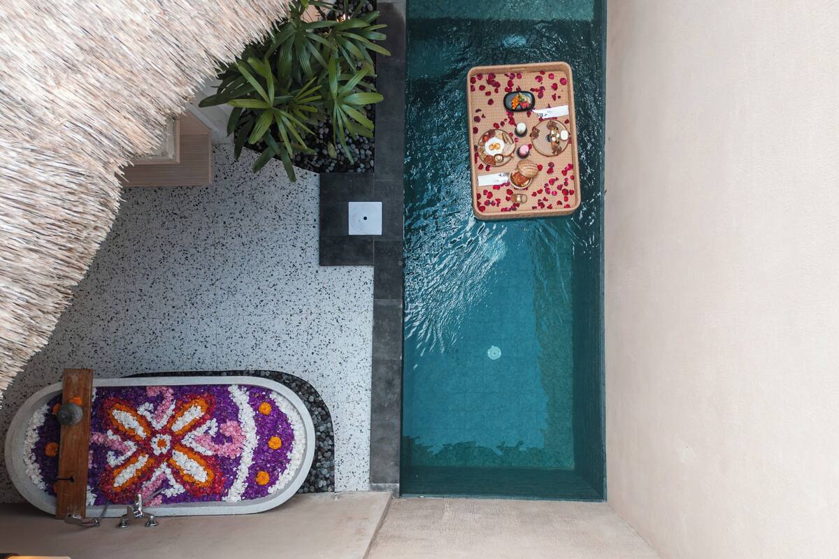 A pool area with a decorative mat, a thatched roof, and a plant.