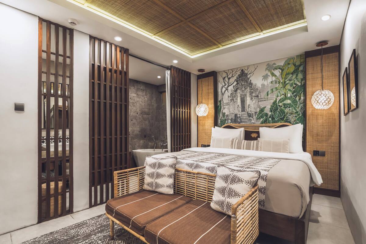 A modern bedroom with a large bed, a wooden partition, a rattan chair, and a mural on the wall.