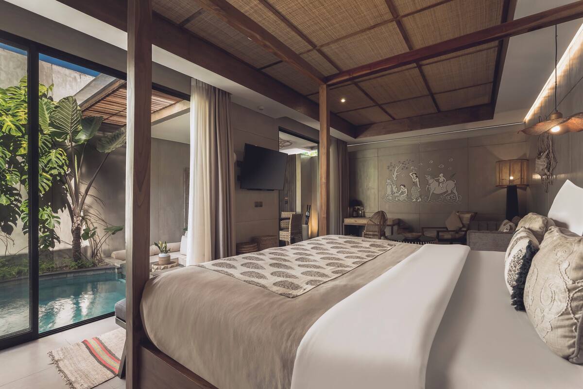 A bedroom with a large bed, a TV, a dining area, and a view of a swimming pool.