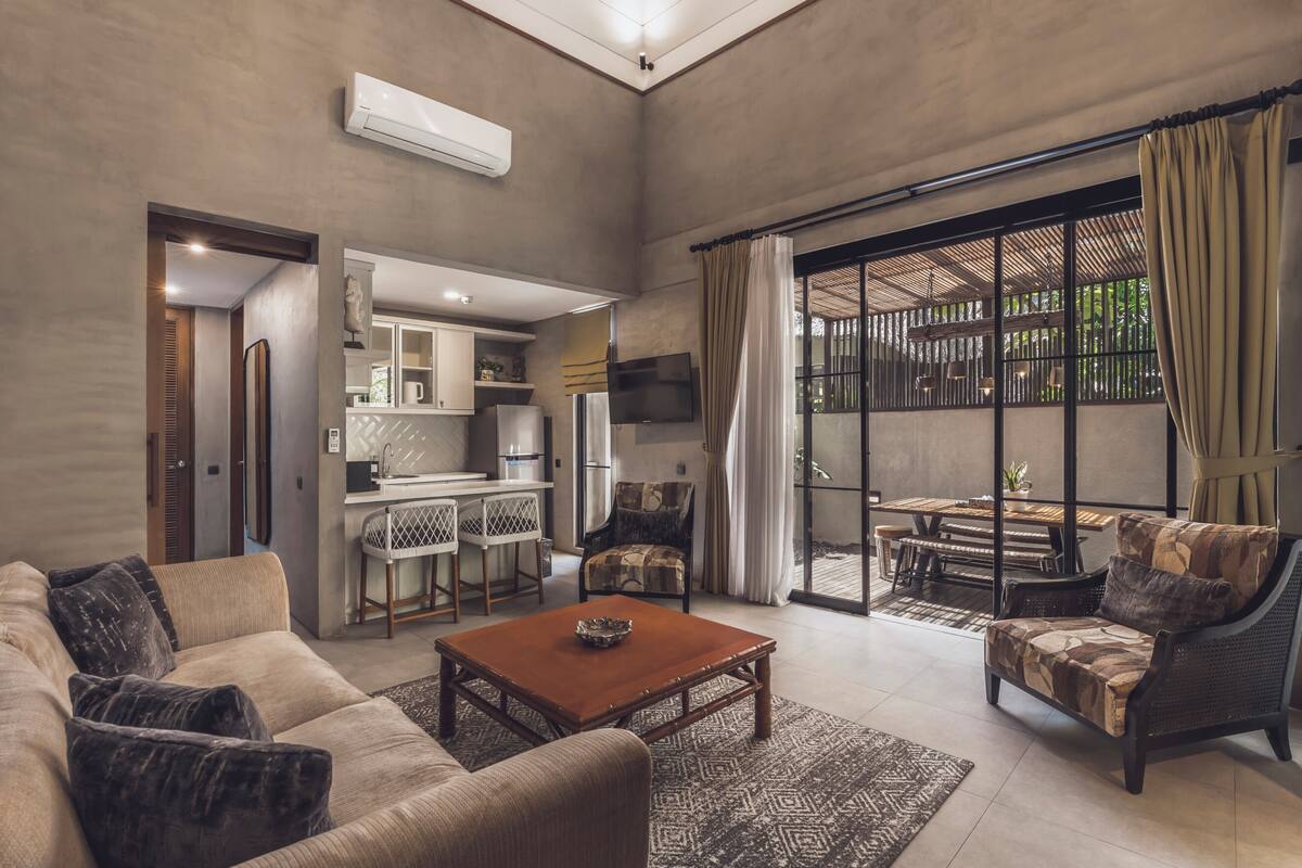 A spacious living room with a sofa, armchair, coffee table, and a dining area with a table and chairs.