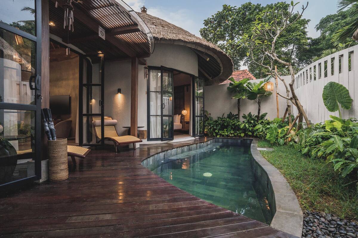 A modern house with a swimming pool, wooden deck, and lush greenery.