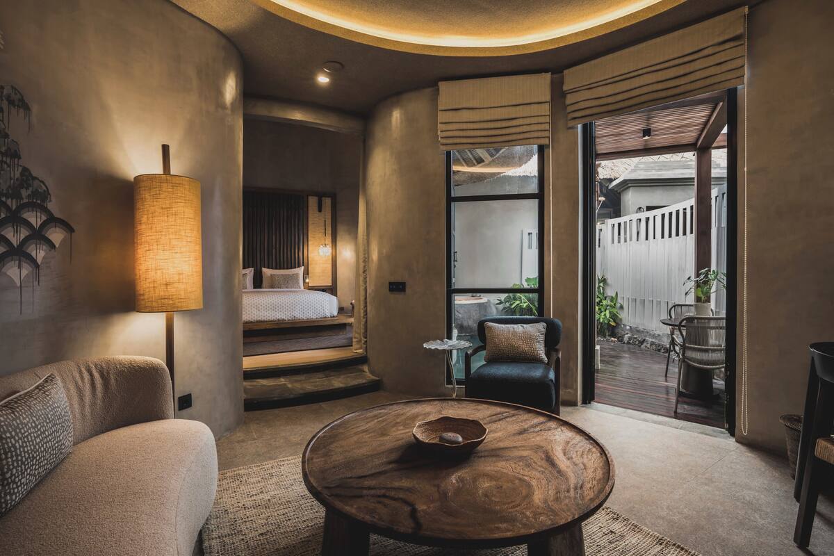 A modern hotel room with a cozy seating area, a large bed, and a view of the outdoor patio.