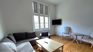 A living room with a sofa, a coffee table, a TV, and a chair. - Castle Tower Apartment 9 - Hohendorf Castle (Groß Mohrdorf)