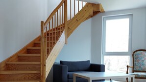 A staircase with wooden railings, a blue sofa, a white coffee table, and a floral-patterned chair in a room with hardwood flooring and a large window. - Castle Tower Apartment 9 - Hohendorf Castle (Groß Mohrdorf)