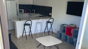 Una cocina moderna con una isla central, un área de comedor con mesa y sillas, un sofá y un televisor montado en la pared.