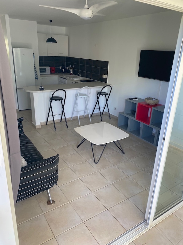 A modern kitchen with a central island, a dining area with a table and chairs, a sofa, and a TV mounted on the wall.