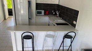 Una cocina moderna con una isla central, tres taburetes de bar, una mesa blanca y un armario rojo.