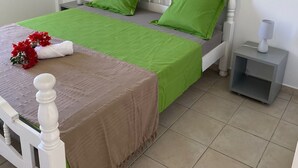 Un dormitorio ordenado con una cama, almohadas verdes, una mesita de noche con una lámpara y un arreglo floral decorativo.