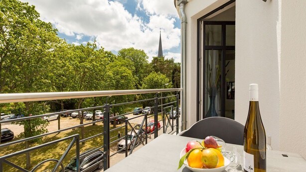 Un balcon avec une table, un panier de fruits et une bouteille de vin.
