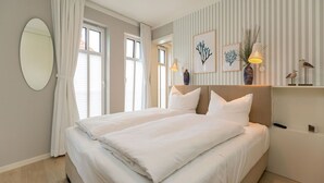 Un lit double avec une literie blanche, un grand miroir rond et un mur à rayures orné d’œuvres d’art encadrées.