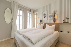 Parivuode valkoisilla vuodevaatteilla, suuri pyöreä peili ja raidallinen seinä, jossa on kehystettyjä taideteoksia.