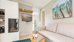Un salon avec un canapé, une table basse sur laquelle repose un livre, une cheminée et un tableau accroché au mur.