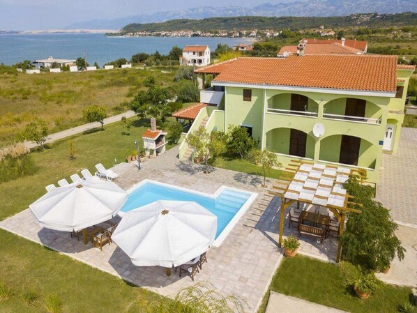 A two-story building with a swimming pool, outdoor seating, and a view of the sea.