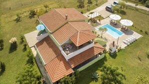 Une maison à deux étages, avec un toit en tuiles, une piscine et un espace salon extérieur.