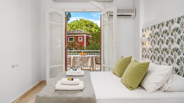 A bedroom with a bed, pillows, and a view of a balcony with a table and chairs. - Pyrgaraki Studios and Apartments (Zakynthos)