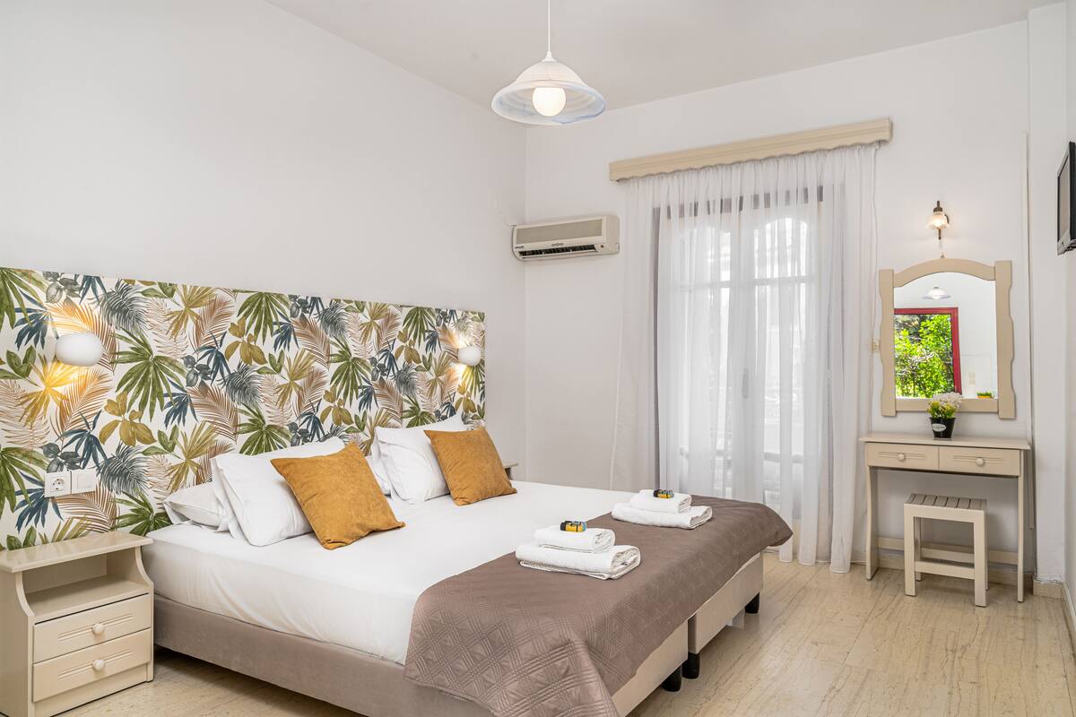 Ein Hotelzimmer mit Bett, Nachttisch, Schreibtisch inklusive Spiegel und einem fenster mit Vorhängen.