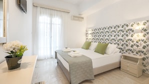 A hotel room with a bed, bedside tables, a potted plant, and a window with curtains. - Pyrgaraki Studios and Apartments (Zakynthos)