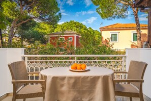 A balcony with wicker chairs and a table, a plate of oranges, and a red building in the background. - Pyrgaraki Studios and Apartments (Zakynthos)