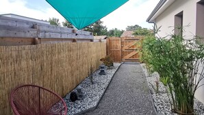 Un'area patio con un pergolato, una recinzione in legno, un piccolo giardino e mobili da esterno.