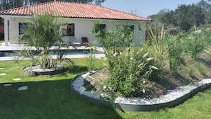 Una casa con tetto in tegole rosse, una piscina e un giardino curato con varie piante e un piccolo patio.