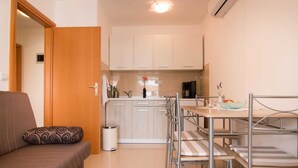 A compact living space with a kitchenette, a dining area with a table and chairs, and a sofa with a patterned cushion. - Apartment 2124/39598 (Istria - Valbandon), 800m from the beach (Valbandon)