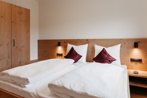 Een net opgemaakt bed met witte lakens en twee kussens, een houten hoofdbord en een nachtkastje met een lamp.