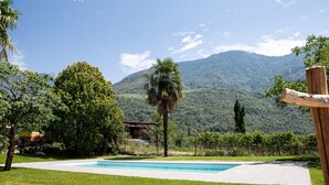 A swimming pool with a mountain backdrop, surrounded by lush greenery and a clear sky. - Holiday Apartment "Torgglbauer 2" with Mountain View, Pool, Terrace & Wi-Fi (Meran)