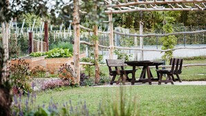 Uma estrutura de pérgula de madeira com uma mesa e cadeiras em um jardim.