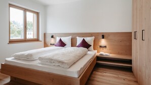 Quarto moderno com cama de madeira, duas luminárias de cabeceira, mesa de cabeceira e janela com vista.