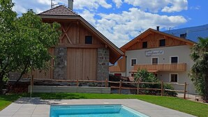 Ein Schwimmbecken mit Holzterrasse, ein Steinhaus mit Ziegeldach und ein Schild mit der Aufschrift 'Corgigebauerhof'.