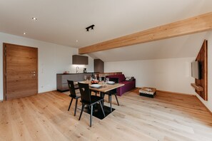 Una cocina moderna con vigas de madera, una zona de comedor con mesa y sillas, y un sofá púrpura.