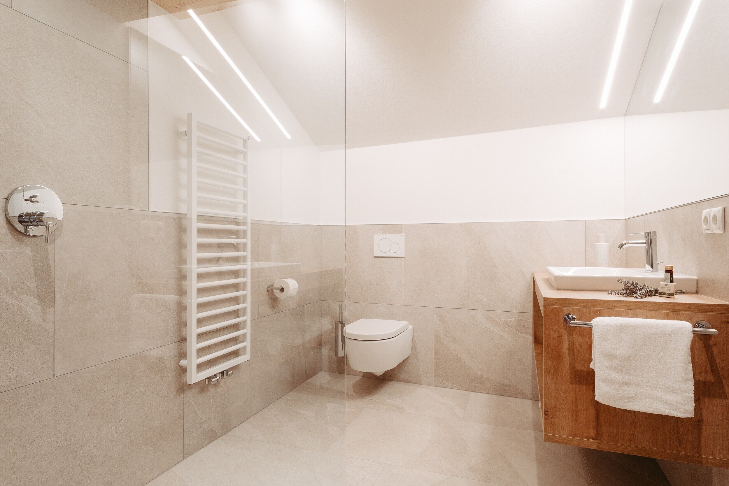 Een moderne badkamer met toilet, wastafel, handdoekhouder en een douchecabine van glas.