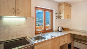 A kitchen with a built-in stove, a sink, wooden cabinets, and a window with a view of a mountainous landscape. - Holiday Apartment 'Thusnelda C' with Mountain View, Balconies & Wi-Fi (Seis am Schlern)