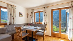 A dining area with a wooden table, chairs, and a view of mountains through large windows. - Holiday Apartment 'Thusnelda C' with Mountain View, Balconies & Wi-Fi (Seis am Schlern)