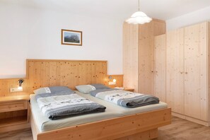 A wooden bed with two pillows, a bedside table, a wall-mounted light, and a framed picture.