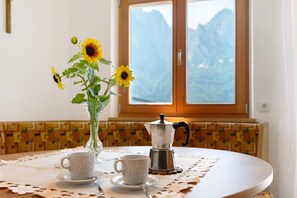 A table with a coffee maker, two cups, and a vase with sunflowers.