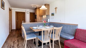 A dining area with a wooden table, blue cushioned bench, and a red sofa. - Holiday Apartment 'Thusnelda A' with Mountain View, Balcony & Wi-Fi (Seis am Schlern)