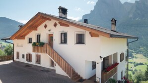 A two-story building with a wooden staircase, a balcony with flowers, and a mountain view. - Holiday Apartment 'Thusnelda A' with Mountain View, Balcony & Wi-Fi (Seis am Schlern)