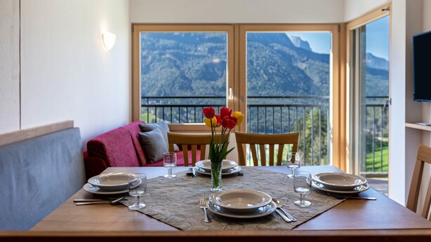 A dining table set for four with a mountain view, a vase with flowers, and a balcony with a view. - Holiday Apartment 'Thusnelda A' with Mountain View, Balcony & Wi-Fi (Seis am Schlern)